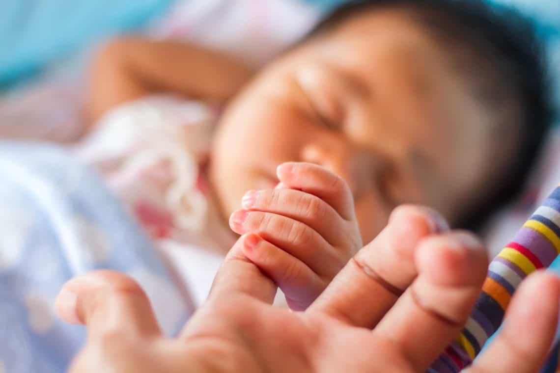 A newborn baby holding his parent's finger
